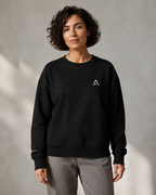 Self Made Club Form Organic Crew in black on an alternate female model, showing the left chest mark, relaxed fit and right wrist embroidery. AI-generated styling visualization.