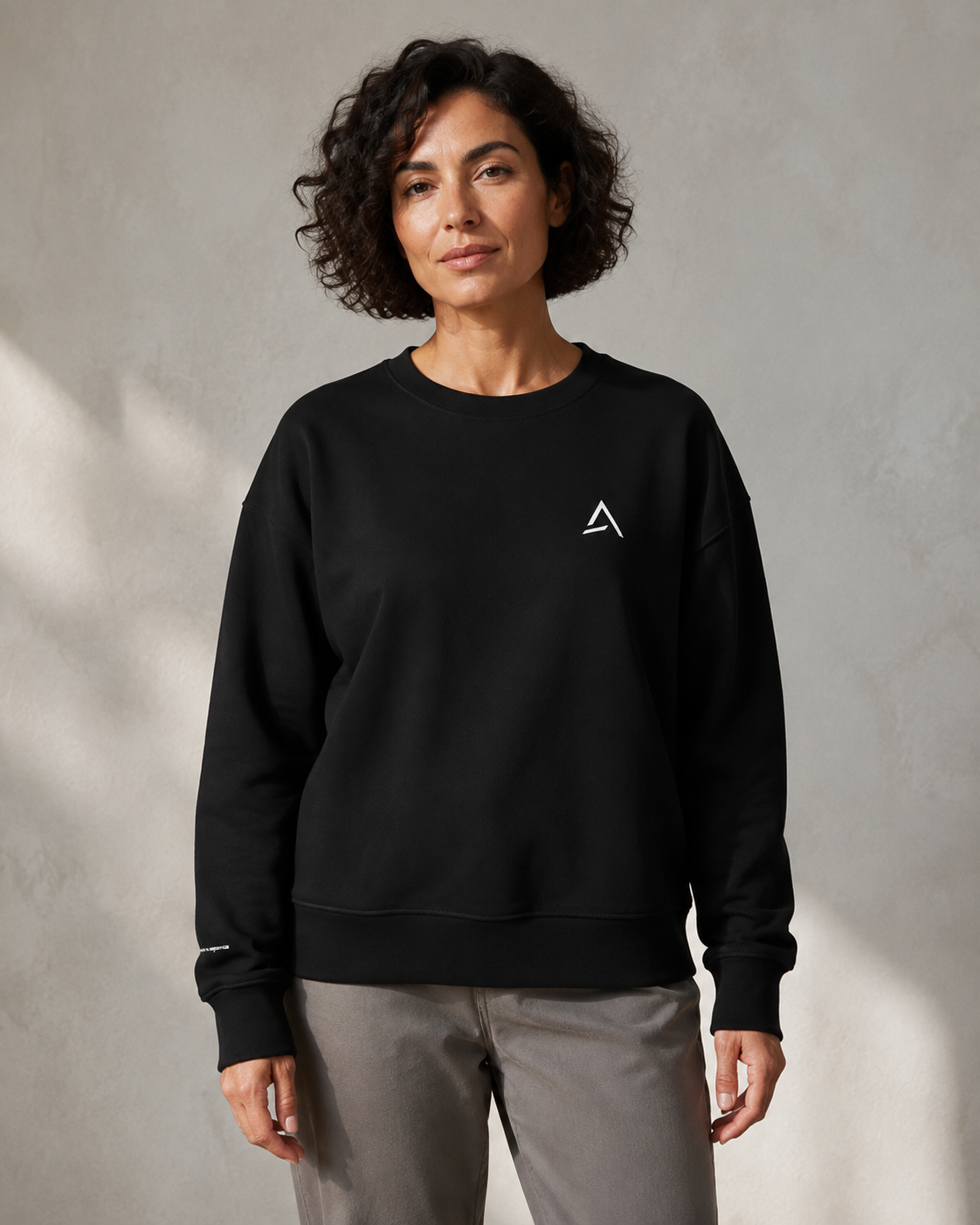 Self Made Club Form Organic Crew in black on an alternate female model, showing the left chest mark, relaxed fit and right wrist embroidery. AI-generated styling visualization.